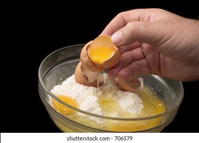 Hand breaking an egg into a glass bowl with flour, black background - Powered by Shutterstock