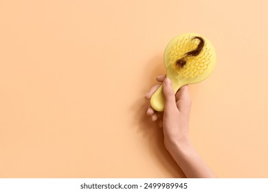 Mano con el cepillo y el grupo de pelo en forma de signo de interrogación sobre fondo beige. Concepto de pérdida de cabello