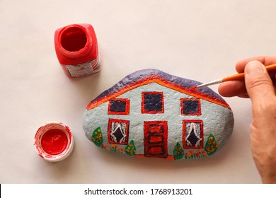 hand with brush painting stone as stylized home, white background and copy space