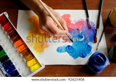 hand with brush painting with watercolor abstract stains