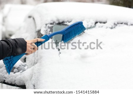 hand with brush removing snow from car windshield in winter day. woman cleaning snow from car. woman is sweeping off snow from her car after snowfall