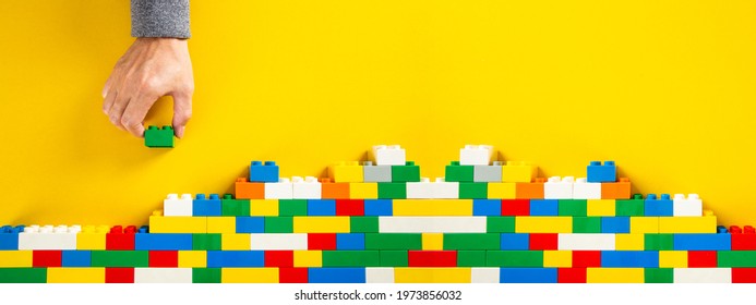 hand building up a wall by stacking up colorful plastic block