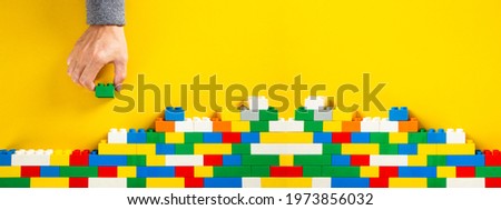 hand building up a wall by stacking up colorful plastic block