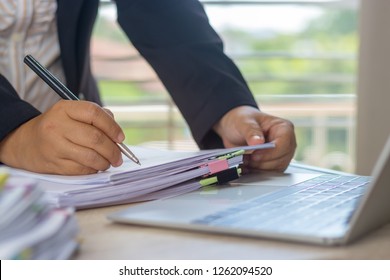 Hand of business analyst holding pen is analyzing graphs about marketing in office. Unfinished paperwork stacked in archive with color binder paper clips. Business and Education concept.