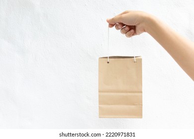 Hand Of Business Woman Hold Brown Paper Shopping Bag On White Concrete Background