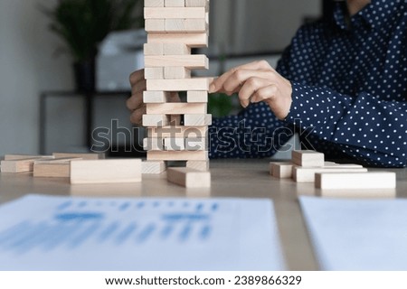 Hand of business woman, leader, entrepreneur, startup company owner building stacked jenga tower, removing wooden block from risky construction. Risk management, challenge, balance metaphor. Close up