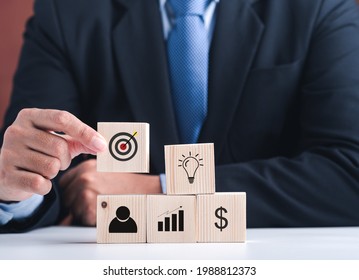 Hand of a businessman arranging wood blocks with the target, ideas, human, graph, and dollar symbol. Close-up photo. Business, strategy, and teamwork concept.