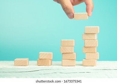 Hand of businessman arranging wooden blocks stacking as step stair on white table, blue background, Ladder of success in business growth concept, copy space - Powered by Shutterstock