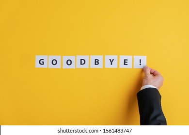 Hand of a businessman assembling a Goodbye sign with white post it papers over yellow background. With copy space.