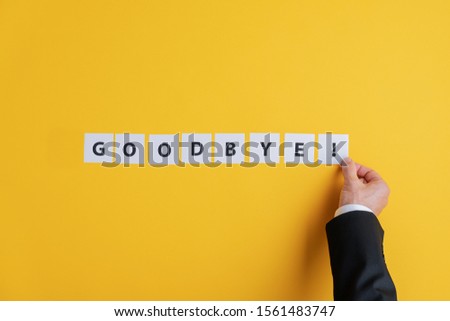 Hand of a businessman assembling a Goodbye sign with white post it papers over yellow background. With copy space.