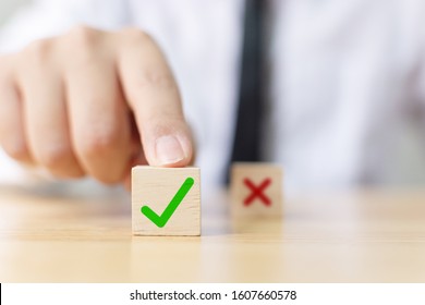 Hand of a businessman chooses checkmark and x sign symbol on wooden cube block
