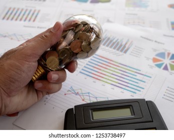 Hand of businessman hold light bulb with coin and calculator on business graph. Concept of Cost reduction and Reduce energy. The use of natural energy