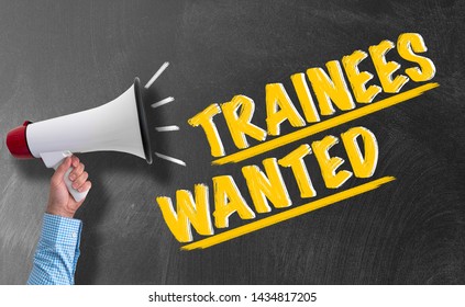 Hand Of Businessman Holding Megaphone Or Bullhorn Against Blackboard With Text TRAINEES WANTED