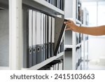 Hand of businessman office worker searching files and paperwork in the archive or document archiving storage room shelf for folder binder finding or data report record or workplace photo concept.