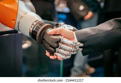 Hand Of A Businessman Shaking Hands With A Android Robot. The Concept Of Human Interaction With Artificial Intelligence.