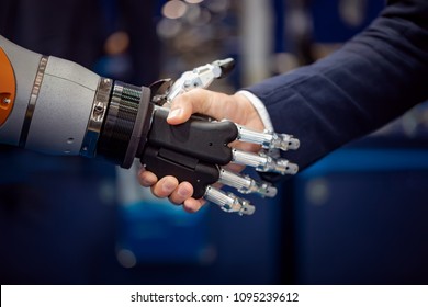 Hand Of A Businessman Shaking Hands With A Droid Robot. The Concept Of Human Interaction With Artificial Intelligence.