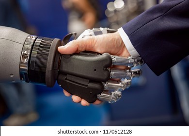 Hand Of A Businessman Shaking Hands With A Droid Robot. The Concept Of Human Interaction With Artificial Intelligence.