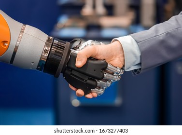 Hand Of A Businessman Shaking Hands With A Robot. The Concept Of Human Interaction With Artificial Intelligence.