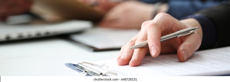 Hand of businessman in suit filling and signing with silver pen partnership agreement form clipped to pad closeup. Management training course, some important document, team leader ambition concept