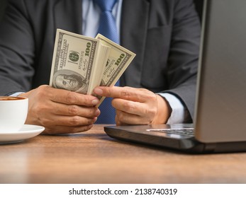 Hand Of A Businessman In A Suit Holding US Dollars Banknote While Sitting In The Office. Close-up Photo. Business And Finance Concept