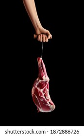 Hand Of A Butcher Holds Raw Leg Of Lamb Over Black Background