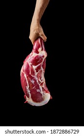 Hand Of A Butcher Holds Raw Leg Of Lamb Over Black Background