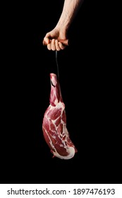 Hand Of A Butcher Holds Raw Leg Of Lamb Over Black Background