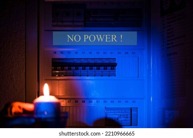 Hand With Candle In Darkness Room On Electricity Switch Box. Power Outage, Blackout, No Power Concept.