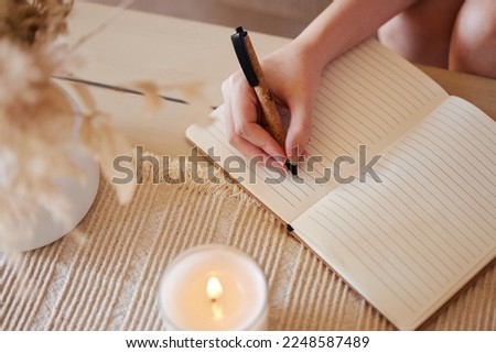 Hand, candle and woman writing in journal with top view for calm, peace mindset and relax morning routine in home. Hands, notebook and diary planning goals, idea vision or creative writer lifestyle