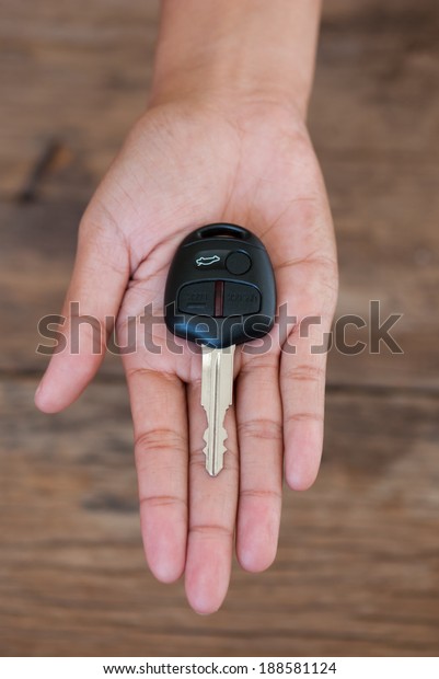 Hand with a car key on\
wood background