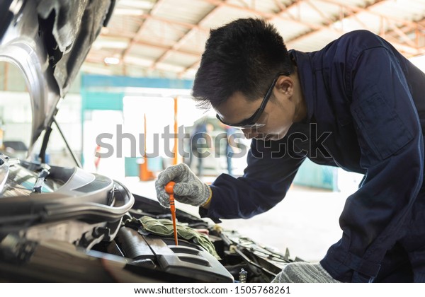 Hand of car mechanic check engine oil for\
maintenance in garage service\
car.