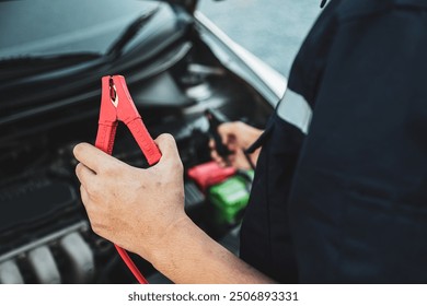 Hand car mechanic holding car booster cables for jump start car for empty battery dead and low voltage power problem or fix and service maintenance accident assistance engine doesn't start. - Powered by Shutterstock