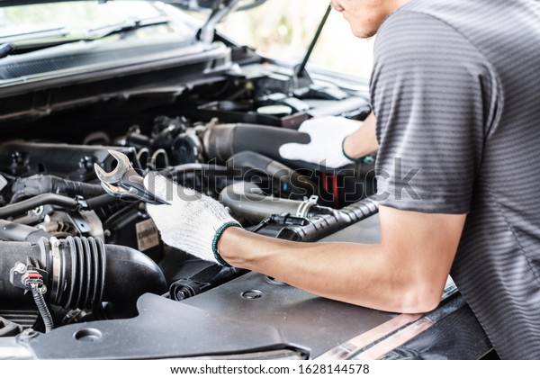 Hand of car mechanic or technician\
holding wrenches near car open hood. Car service\
concept.