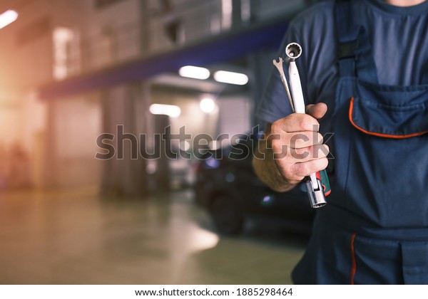 The hand of a car repairman with\
keys and a special tool on the background of the service area. A\
mechanic in a car service station in uniform. Copy\
space