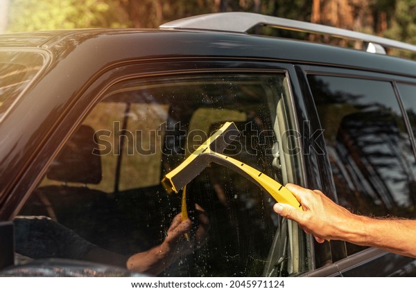 Hand\
with car rubber scraber clean auto window\
outside.