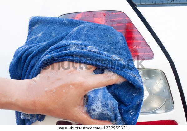 Hand of the car wash with blue cloth at the tail\
lights white car.