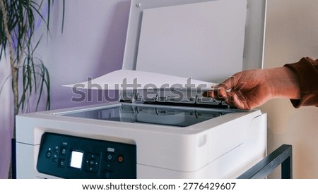 A hand carefully inserts a sheet of paper into the scanner lid of a white multifunction printer, preparing for a copy or scan job