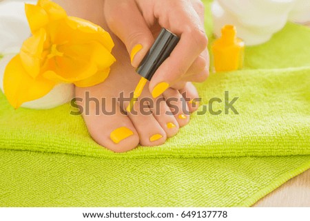 Hand cares about a foot nails. Pedicure beauty salon. Nail varnishing in yellow color. Spring and summer atmosphere with yellow and green colors.