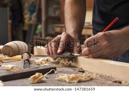 hand of a carpenter taking measurement of a wooden plank