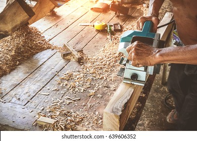 Hand of carpenter using electric planer with wooden plank in carpentry workshop