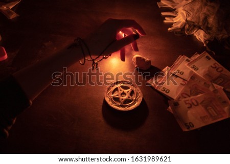 Hand casting magic spell. Witch doing ritual for money. Pentagram, stones and other occult equipment on the table. 