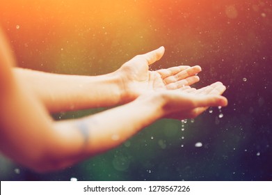 hand catching rain drops on blurred background. Woman hands praying for blessing from god on sunset. Empowerment, sacred forgiveness, positive arm energy, good morning, reborn change calm zen concept.