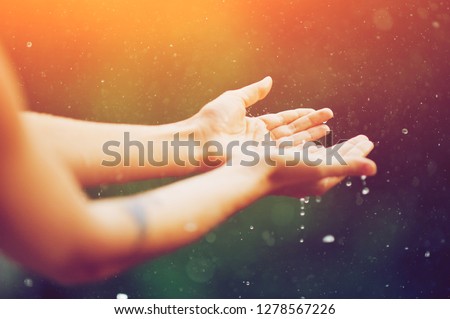 hand catching rain drops on blurred background. Woman hands praying for blessing from god on sunset. Empowerment, sacred forgiveness, positive arm energy, good morning, reborn change calm zen concept.