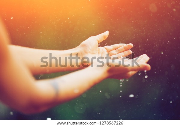hand catching rain drops on blurred background.\
Woman hands praying for blessing from god on sunset. Empowerment,\
sacred forgiveness, positive arm energy, good morning, reborn\
change calm zen concept.