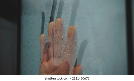 Hand of Caucasian Female Touching Wet Shower Cabin Glass Swiping Water Steam and Droplets