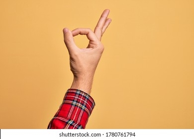 Mano de un joven caucásico que muestra los dedos sobre un fondo amarillo aislado gestando la expresión de aprobación haciendo un símbolo correcto con los dedos