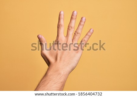 Hand of caucasian young man showing fingers over isolated yellow background counting number 5 showing five fingers