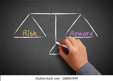 Hand With Chalk Is Drawing Risk And Reward Balance Scale On The Chalkboard.