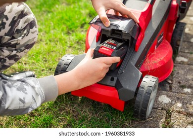 Hand changing accumulator - Teenager changes rechargeable battery in electric lawn mower - Shutterstock ID 1960381933