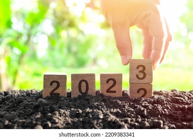 Hand changing year 2022 to 2023 in wooden blocks cubes with growing plant at sunrise. New year 2023, hope, hello and goodbye concept. - Shutterstock ID 2209383341